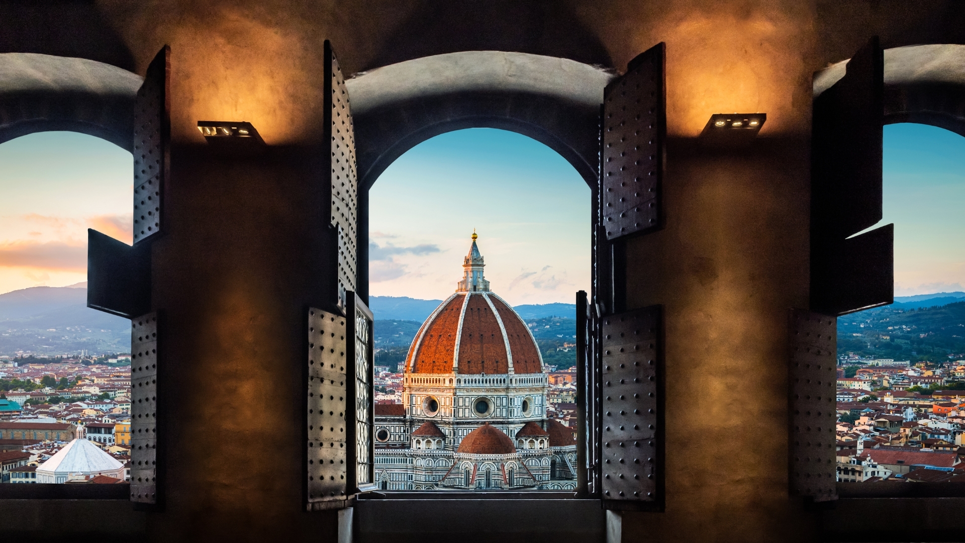 The image shows a view from an old window overlooking the Florence Duomo, also known as the Basilica di Santa Maria del Fiore, with its iconic dome prominently displayed. The scene captures the architectural beauty of the basilica against a backdrop of the city of Florence and the surrounding hills, framed by the window's open shutters.